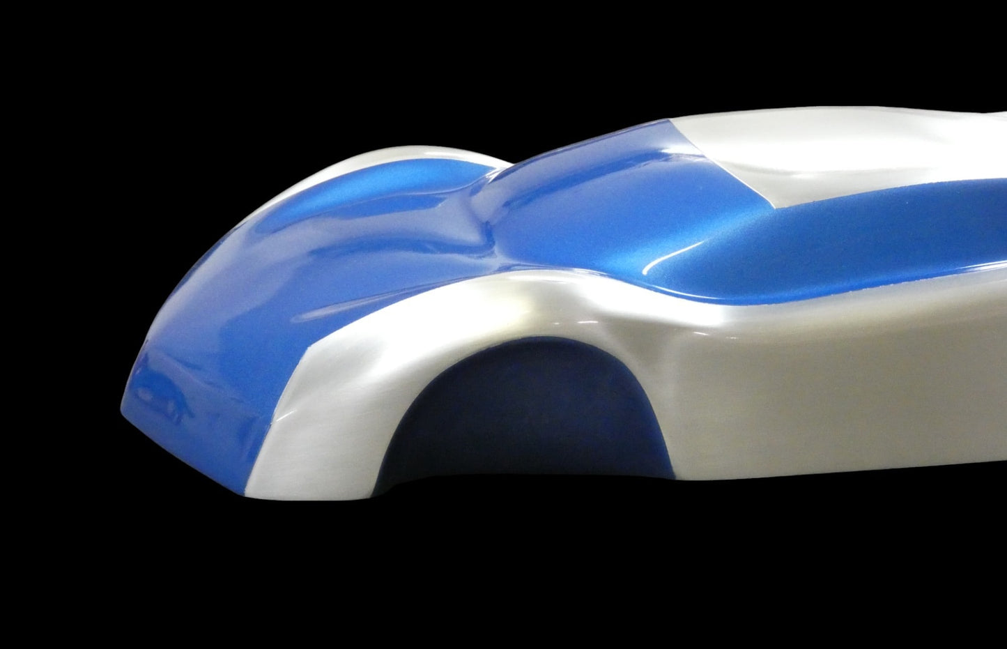 Metal sheet automotive sculpture with silver and gold finish representing V12 supercar, created by Frédéric Girard, limited edition of 8, 45 x 19 cm format. Nose side view showcasing the iconic curves and the meticulous attention to each sculpted detail, a collector’s piece for automotive and fine craftsmanship enthusiasts.
