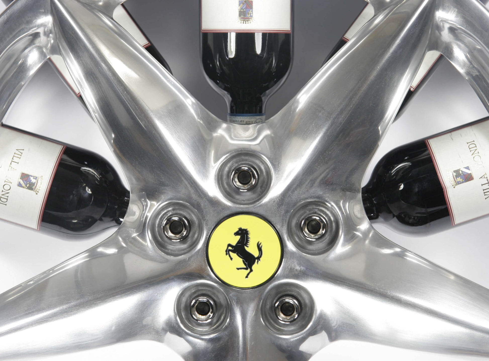 Car wheel rim bottle display stand made from a Ferrari 360 Modena wheel rim. This automotive art object measures 55x24 cm. Custom-made and handcrafted by Car2Art. Ideal for automotive art collectors. It can hold five bottles of wine or spirits. Focus on the Ferrari logo.