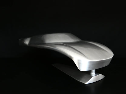 Metal sheet automotive sculpture with raw aluminium representing a Ford GT40 evocation, created by Frédéric Girard, limited edition of 8, 45x19 cm format. Nose 3/4 left view showcasing the iconic curves and the meticulous attention to each sculpted detail, a collector’s piece for automotive and fine craftsmanship enthusiasts.